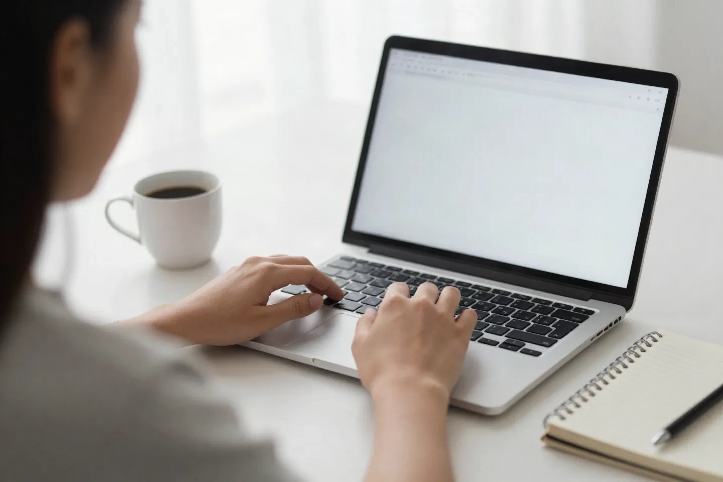 Hands on a laptop keyboard next to a coffee cup and a small notebook