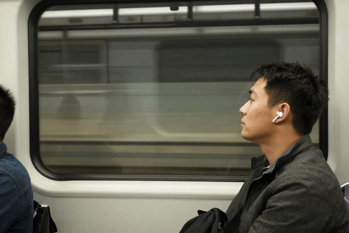 Commuter sitting by a subway train window wearing earbuds, listening to a narrated article