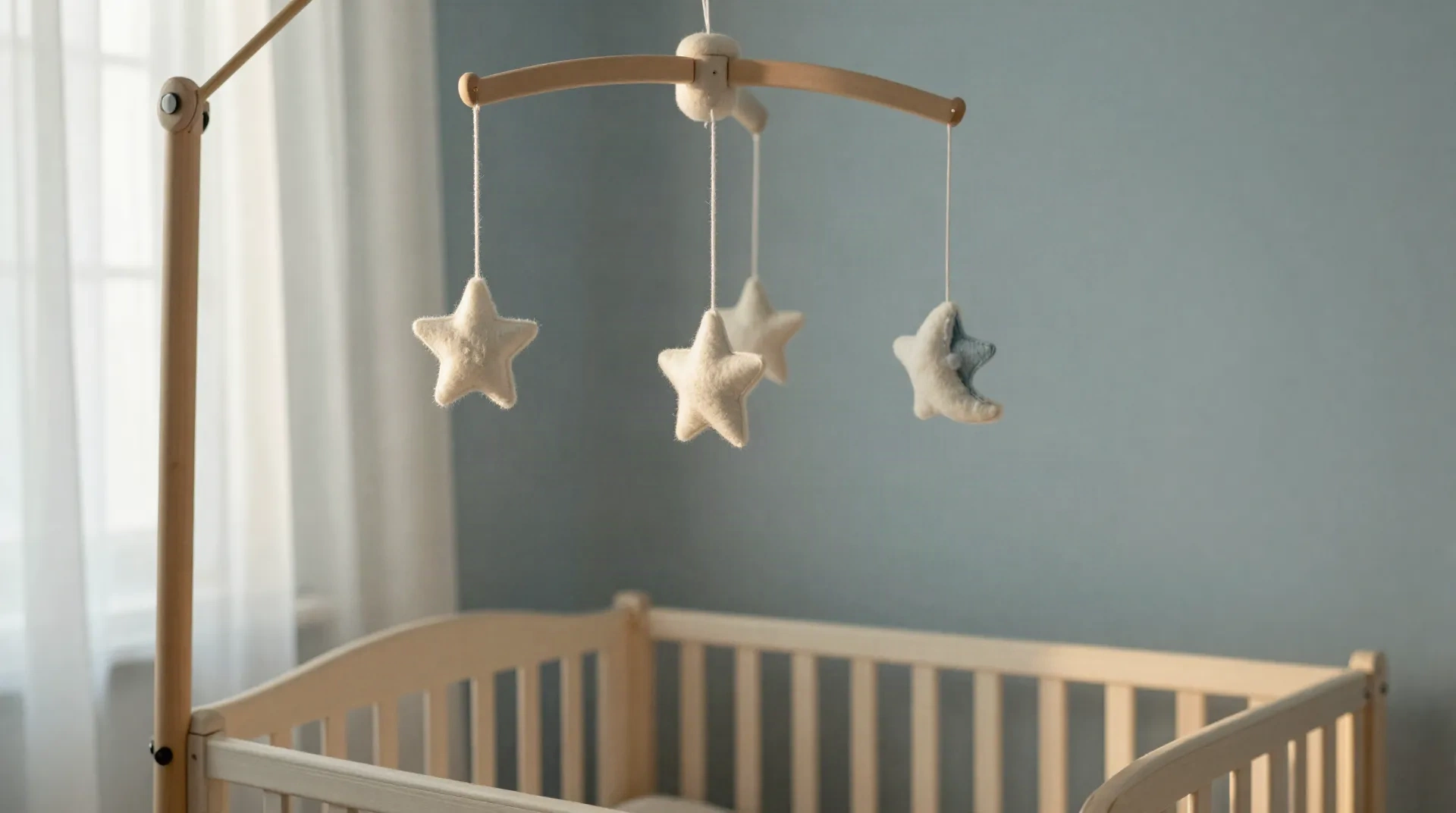 Hölzernes Kinderzimmer-Mobile mit Filzsternen über einem Gitterbett, sanftes Morgenlicht