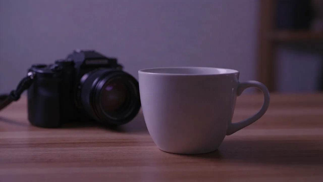 Slightly soft photo of a white ceramic mug and a mirrorless camera on a wooden desk